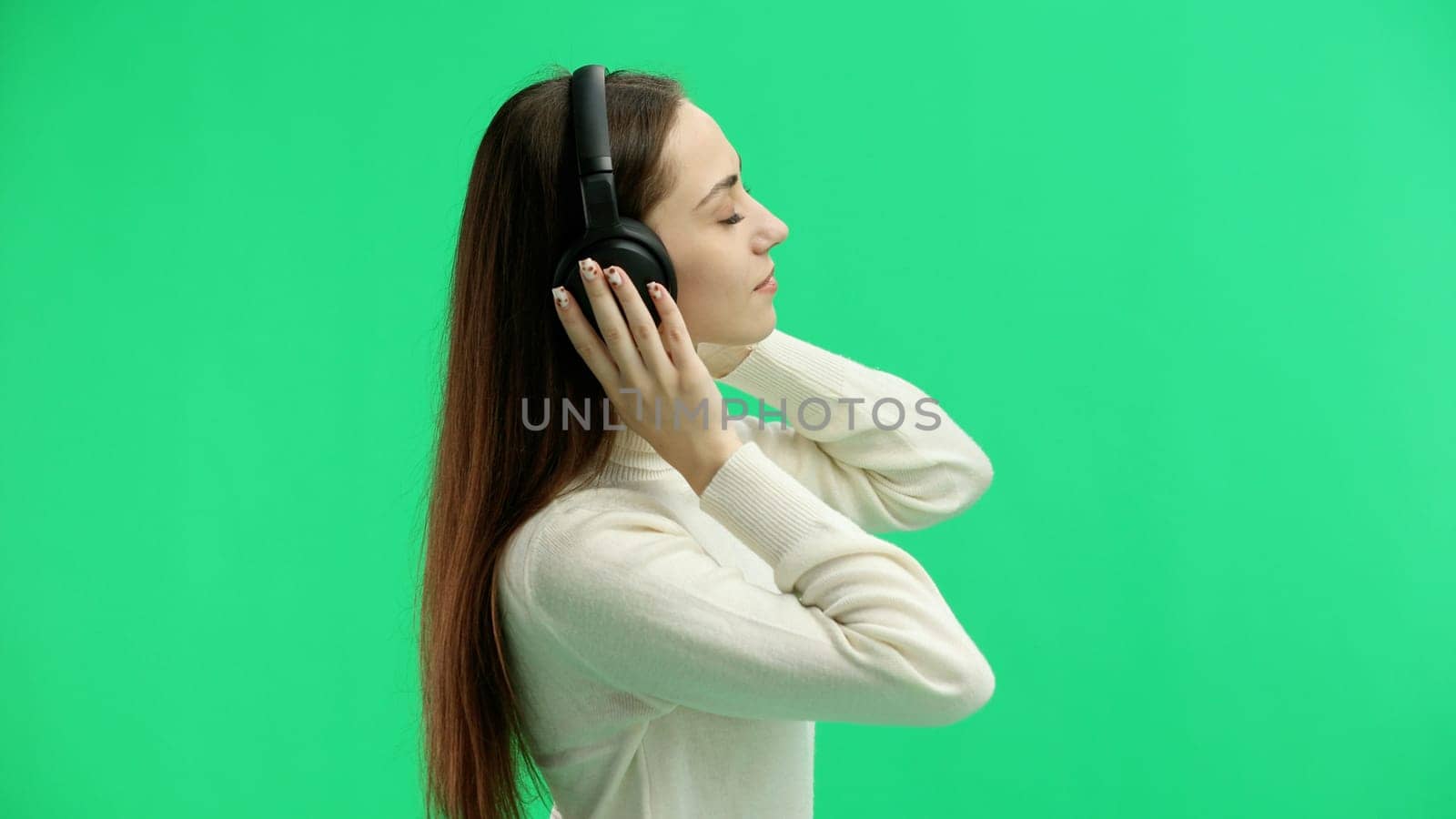 A woman, close-up, on a green background, listening to music with headphones.