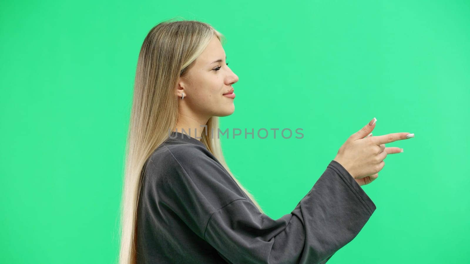 A woman, close-up, on a green background, points to the side.