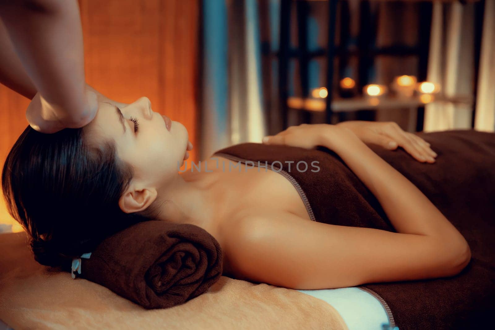 Caucasian woman enjoying relaxing anti-stress head massage and pampering facial beauty skin recreation leisure in warm candle lighting ambient salon spa in luxury resort or hotel. Quiescent