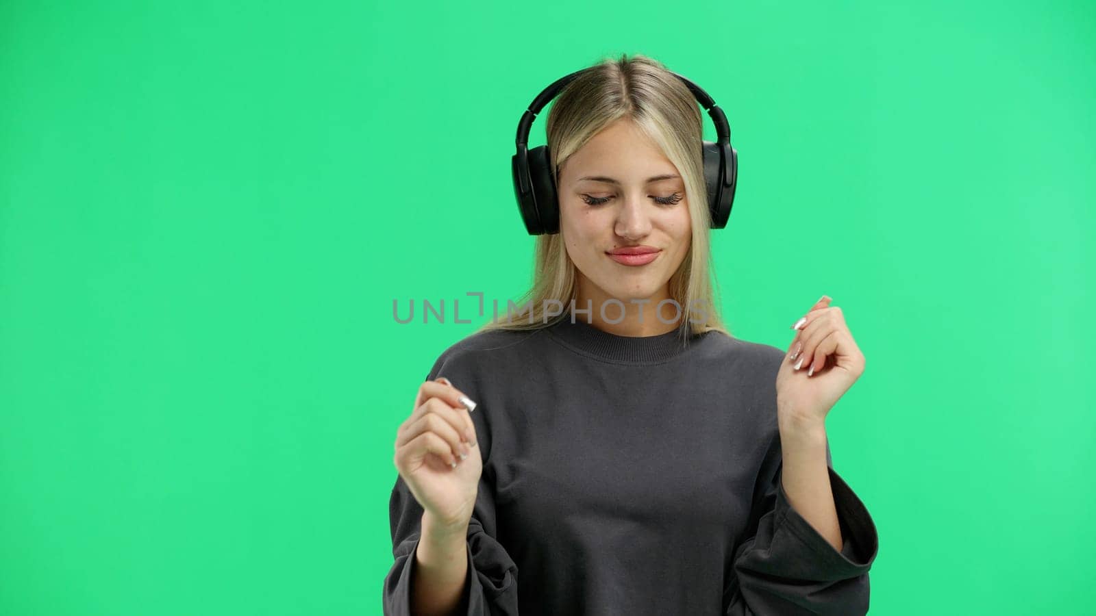 A woman, close-up, on a green background, listening to music with headphones.