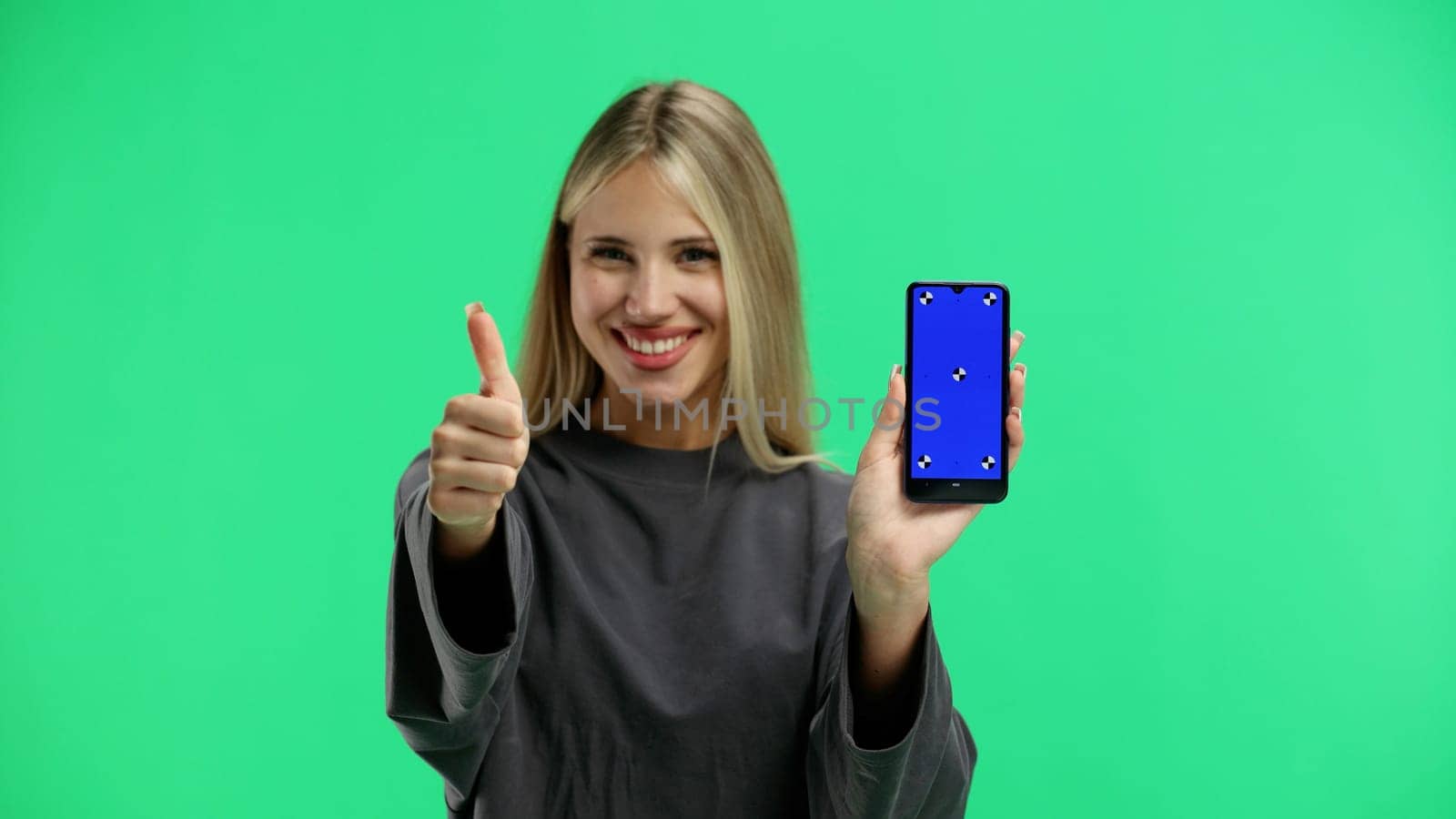 A woman, close-up, on a green background, shows a phone.