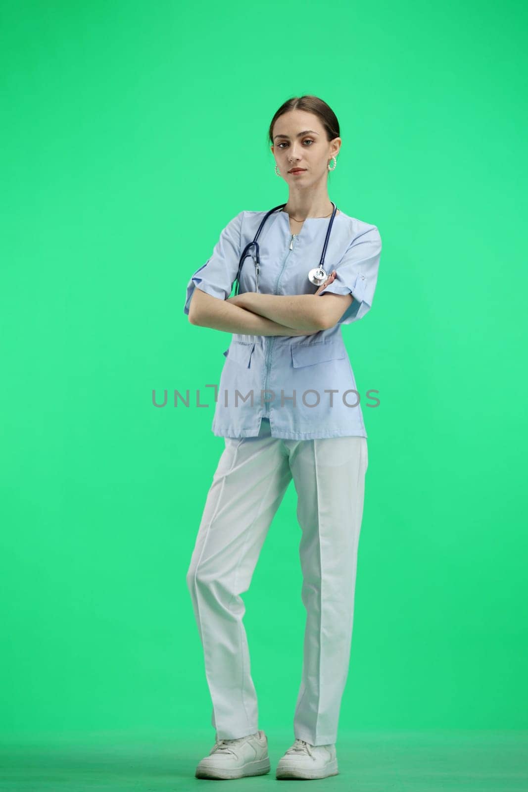 A full-length female doctor on a green background crossed her arms.