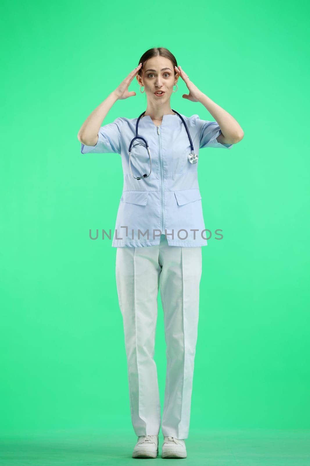 A full-length female doctor on a green background clutched her head.