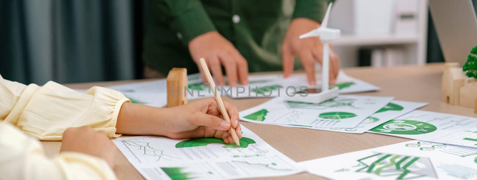 Professional businesswoman attended in green business meeting while male investor presenting about using clean energy on table with environmental document scatter around. Focus on hand. Delineation.