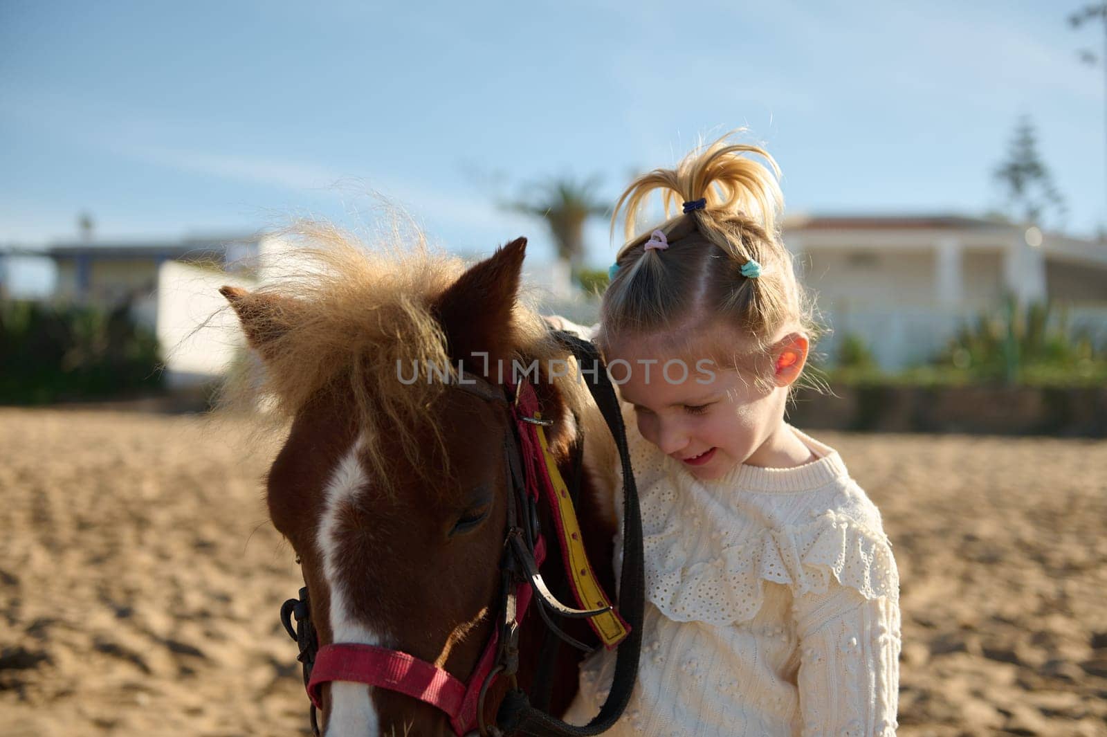 Cute blonde little child girl stroking a pony, smiling and enjoying happy weekend outdoor. Children and love for animals by artgf