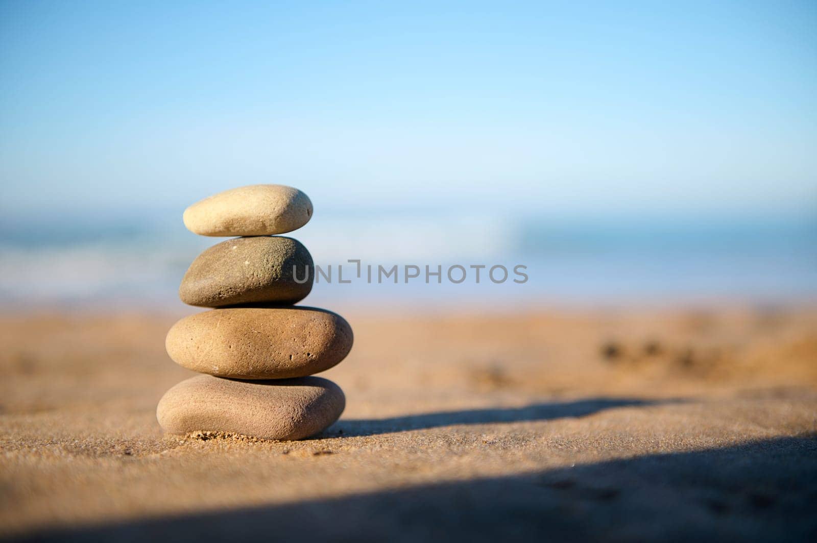Still life with stacked pebbles, stones on the sandy beach against the background of Atlantic ocean with waves breaking on the beach. The concept of harmony and balance. Copy advertising space