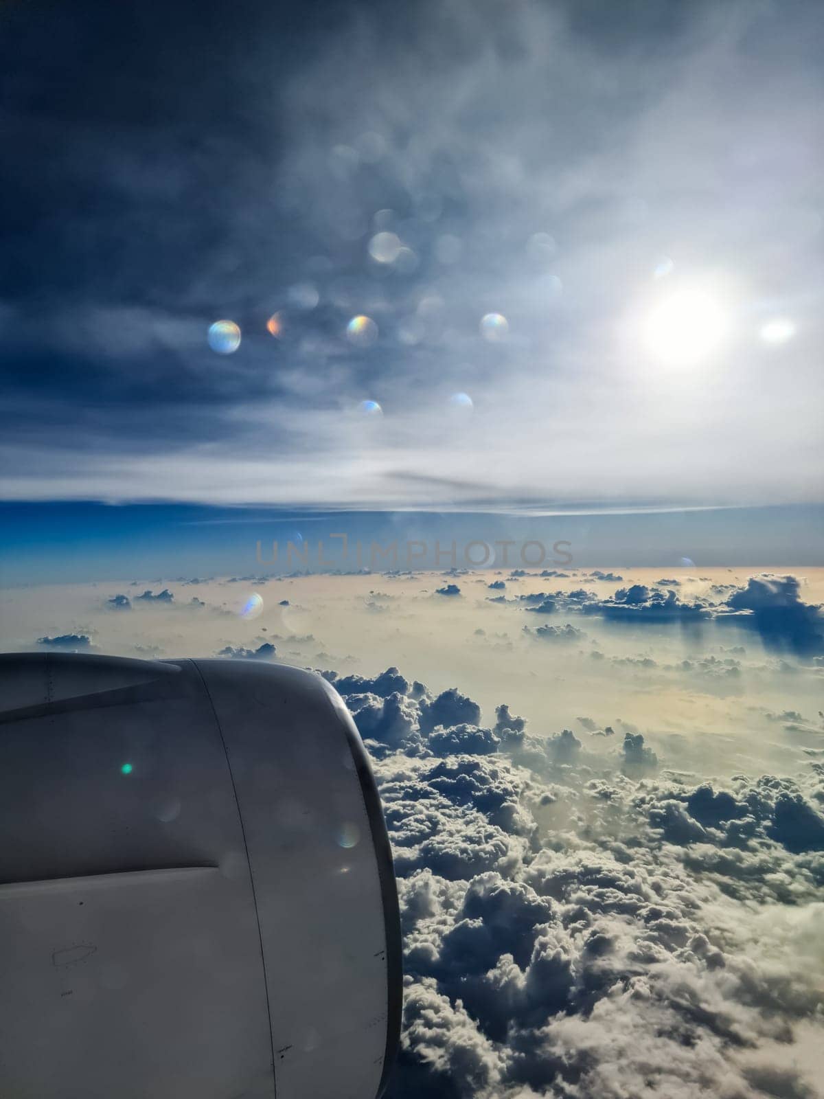 View from an airplane window of the sun and great cloud formations with many small spots on the window. by MP_foto71
