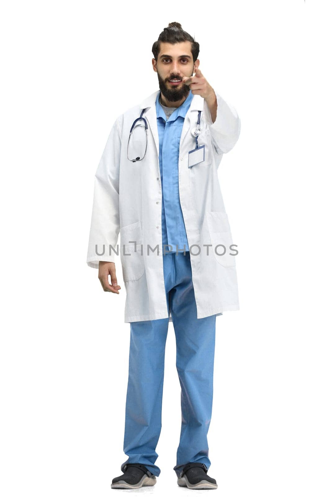 The male doctor, full-length, on a white background, points forward.