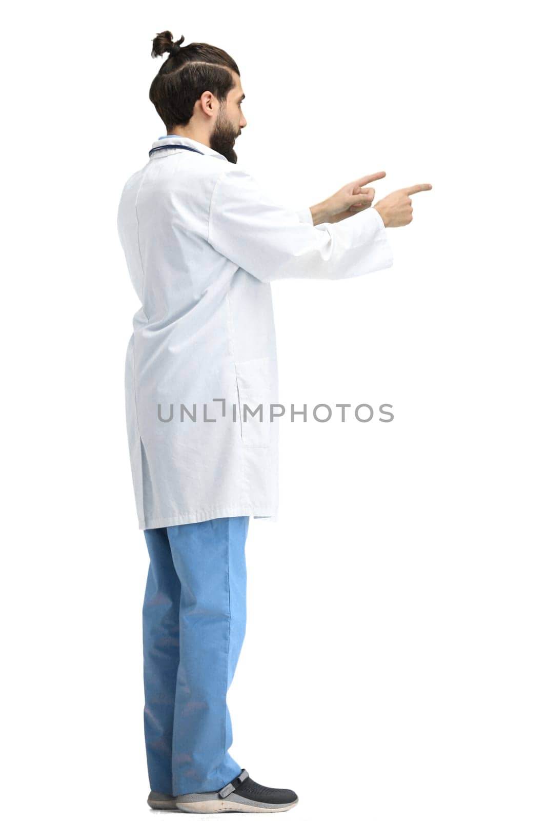 The male doctor, full-length, on a white background, points to the side.