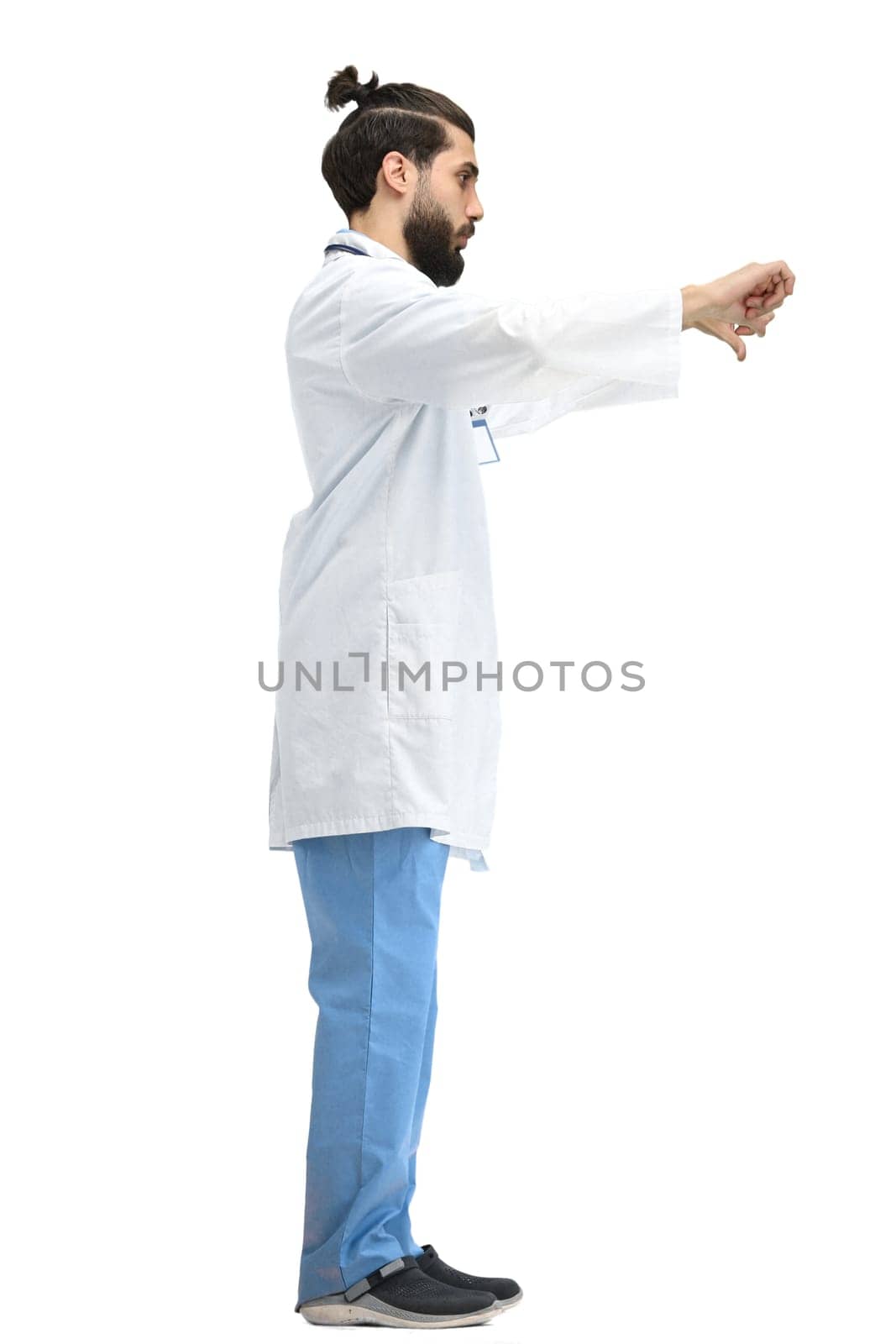 A male doctor, full-length, on a white background, shows his thumbs down.