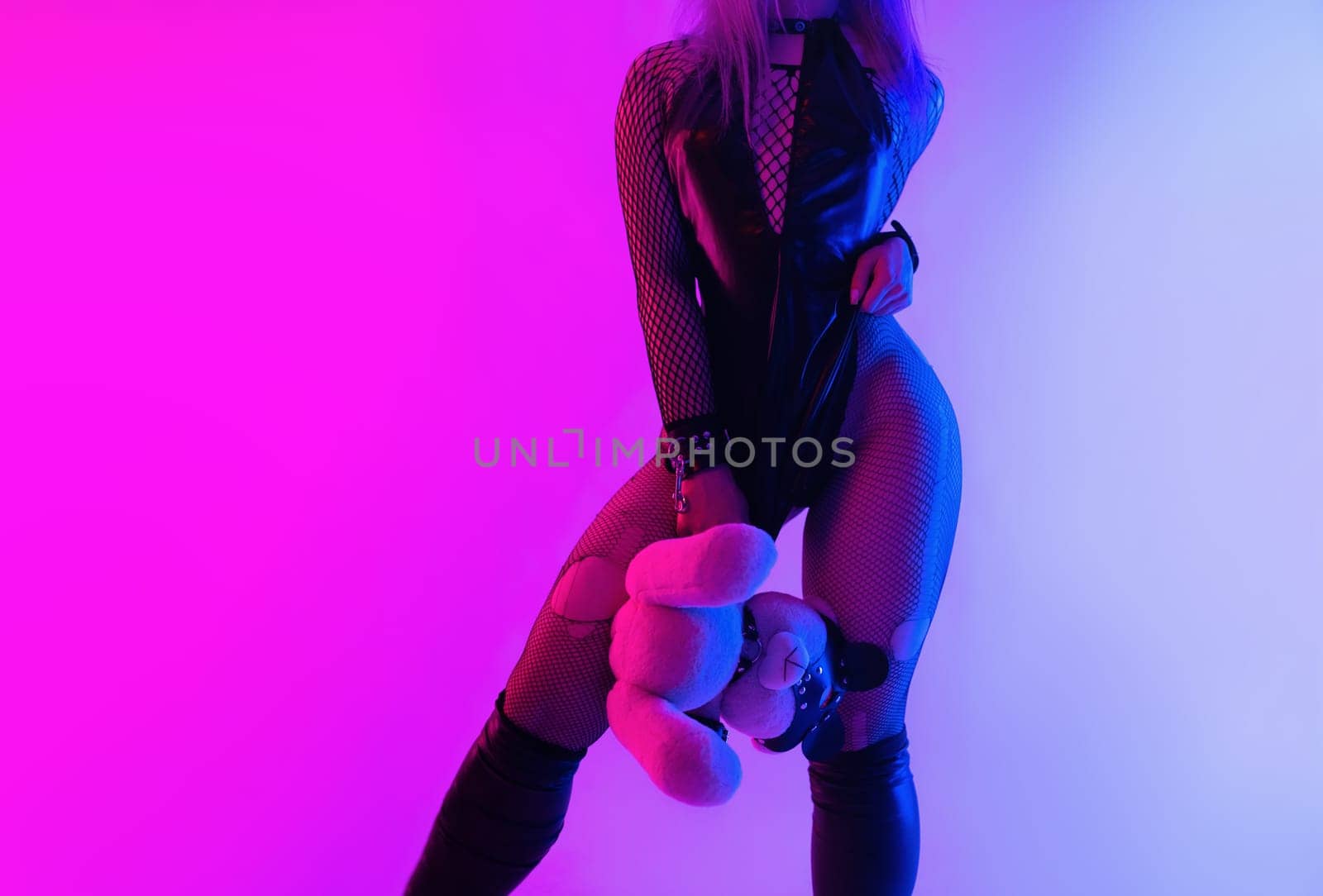 Sexy girl in a latex BDSM mistress dress and a cat mask in neon light on a dark background for sex game