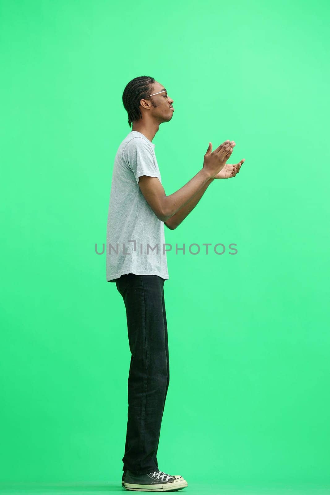 A man in a gray T-shirt, on a green background, in full height, claps.