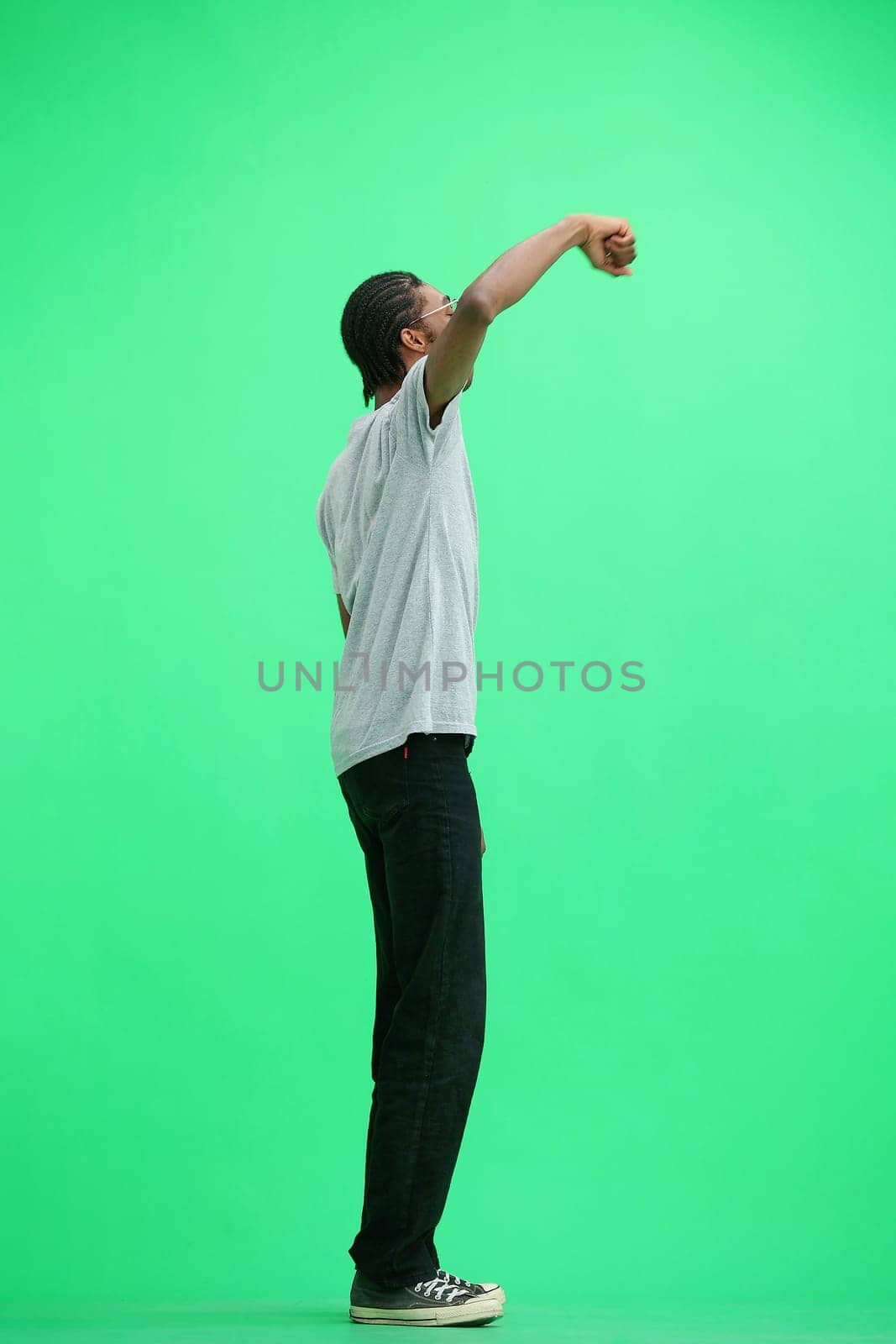 A man in a gray T-shirt, on a green background, in full height, rejoices.