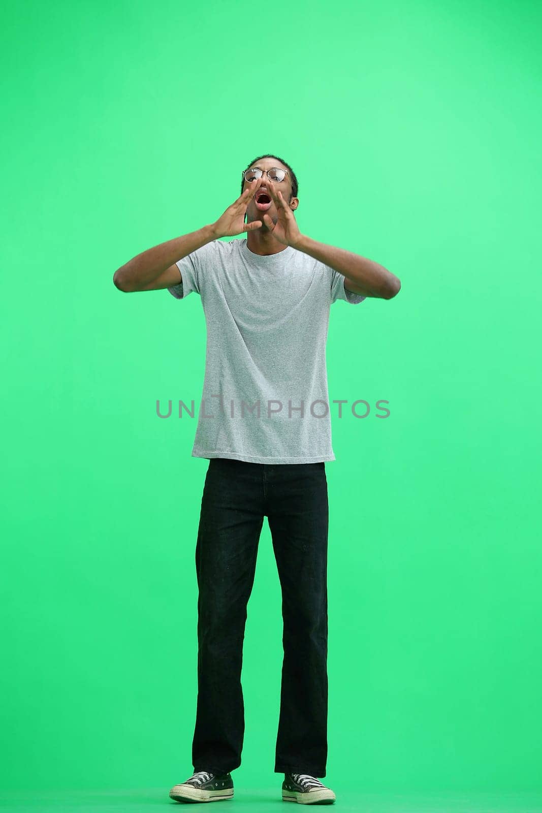 A man in a gray T-shirt, on a green background, in full height, rejoices.