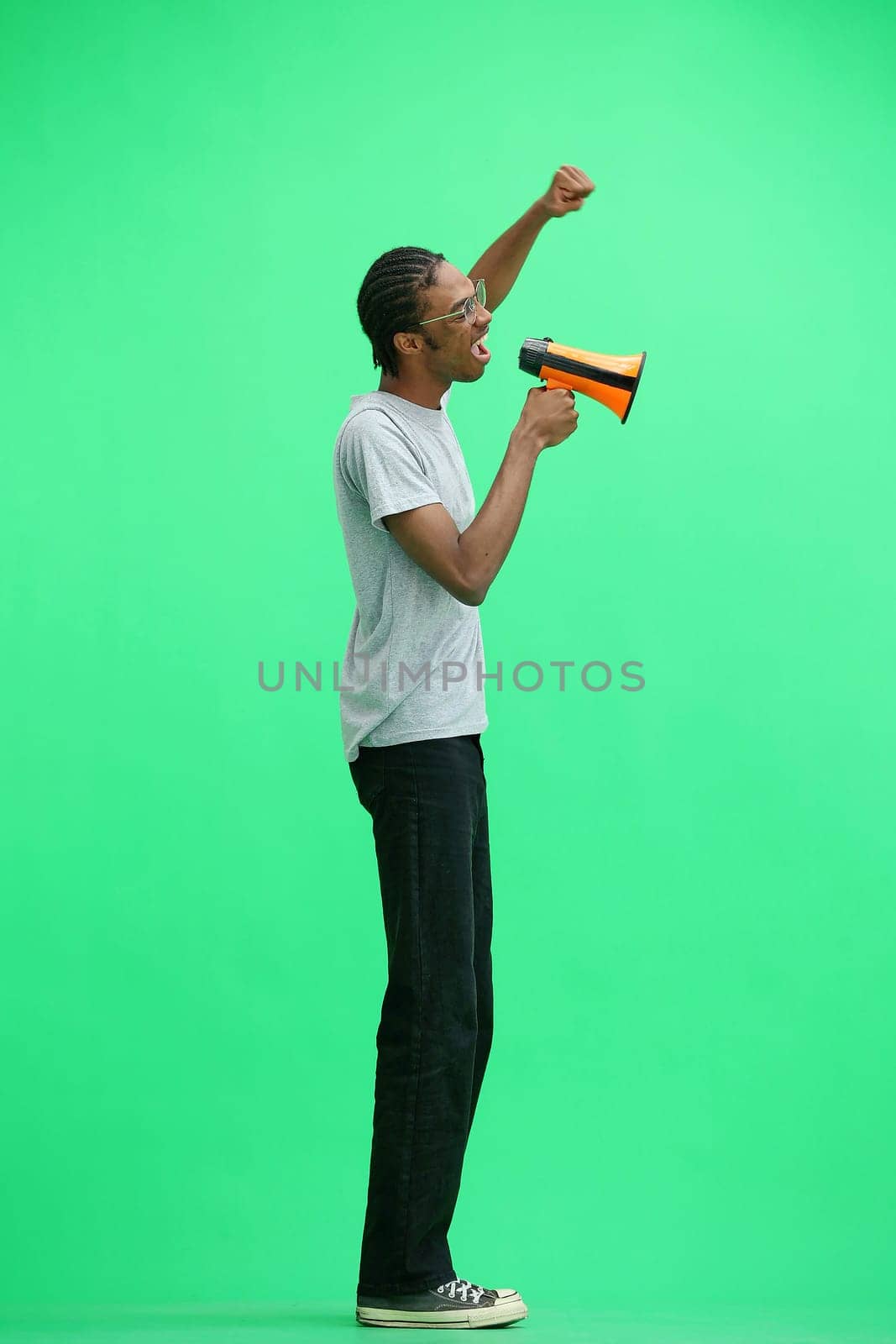 A man in a gray T-shirt, on a green background, full-length, with a megaphone.