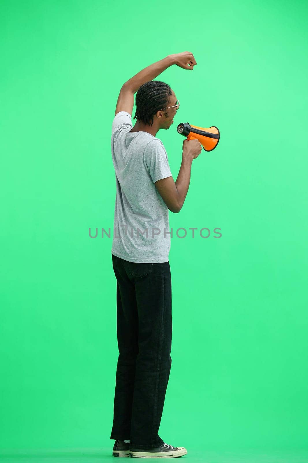 A man in a gray T-shirt, on a green background, full-length, with a megaphone.