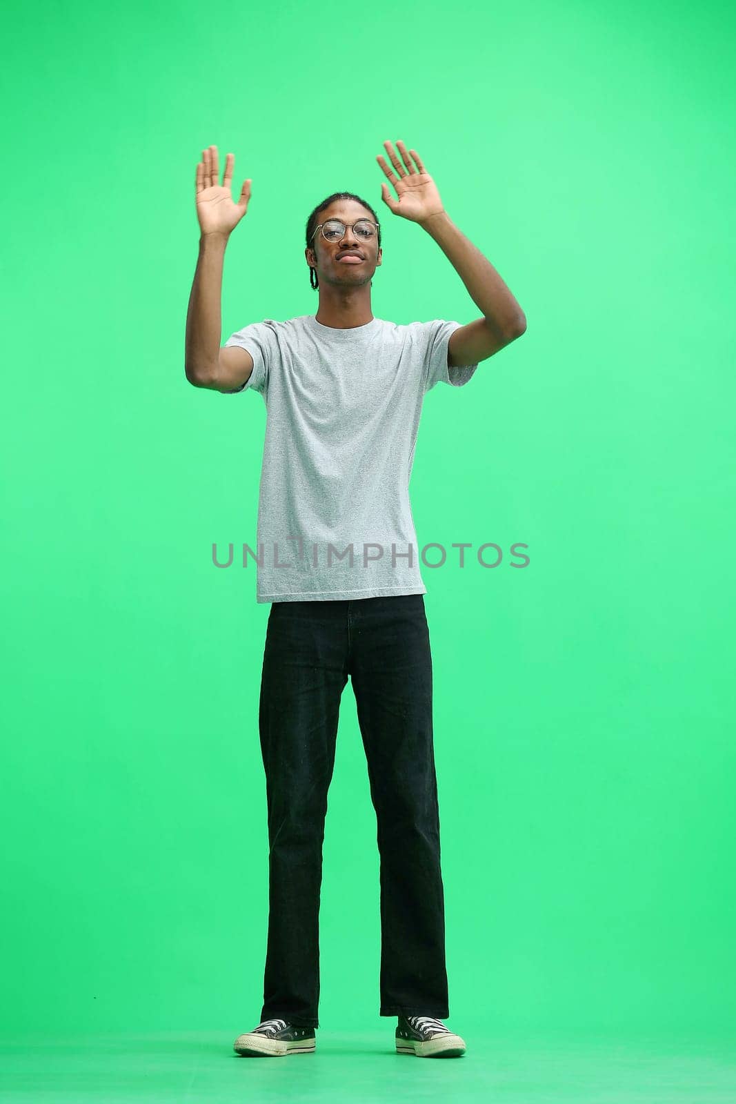 A man in a gray T-shirt, on a green background, standing tall, waving his arms.