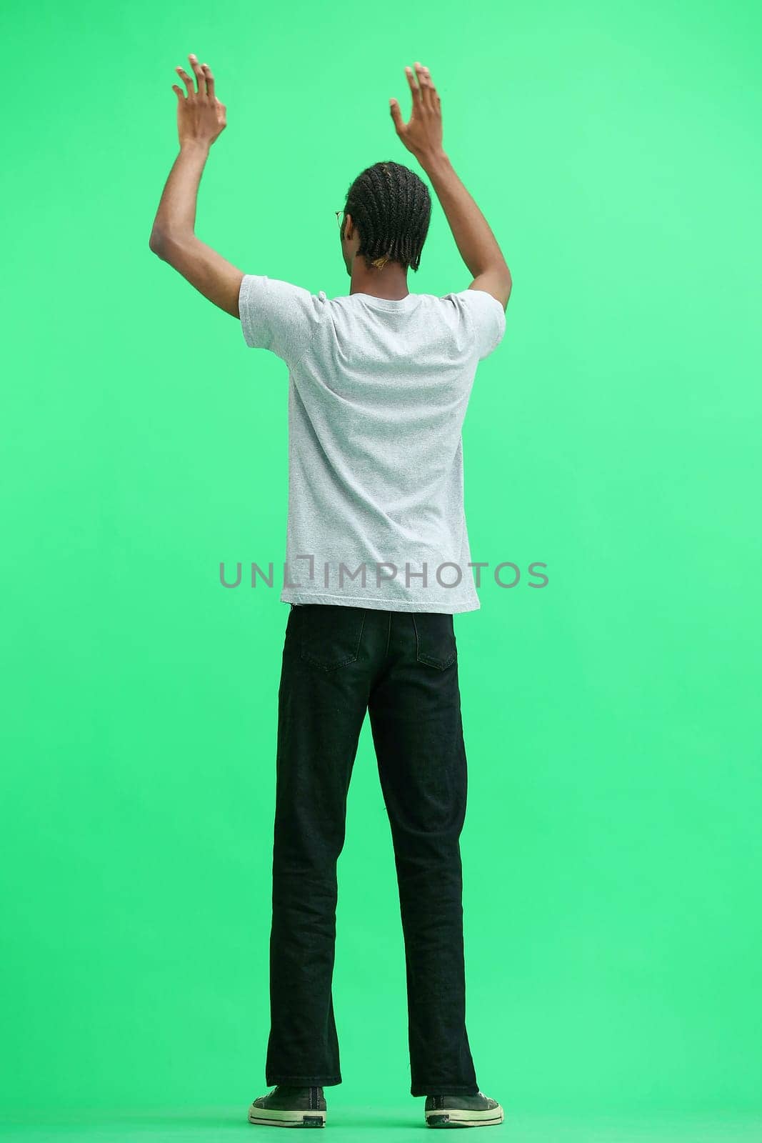 A man in a gray T-shirt, on a green background, standing tall, waving his arms.