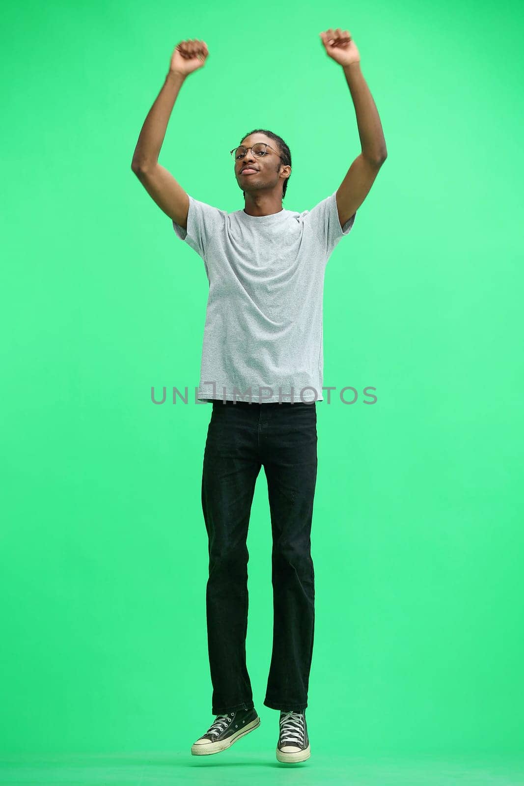 A man in a gray T-shirt, on a green background, full-length, jumps.