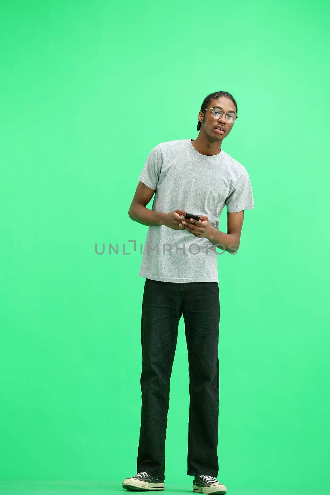A man in a gray T-shirt, on a green background, full-length, with a phone.