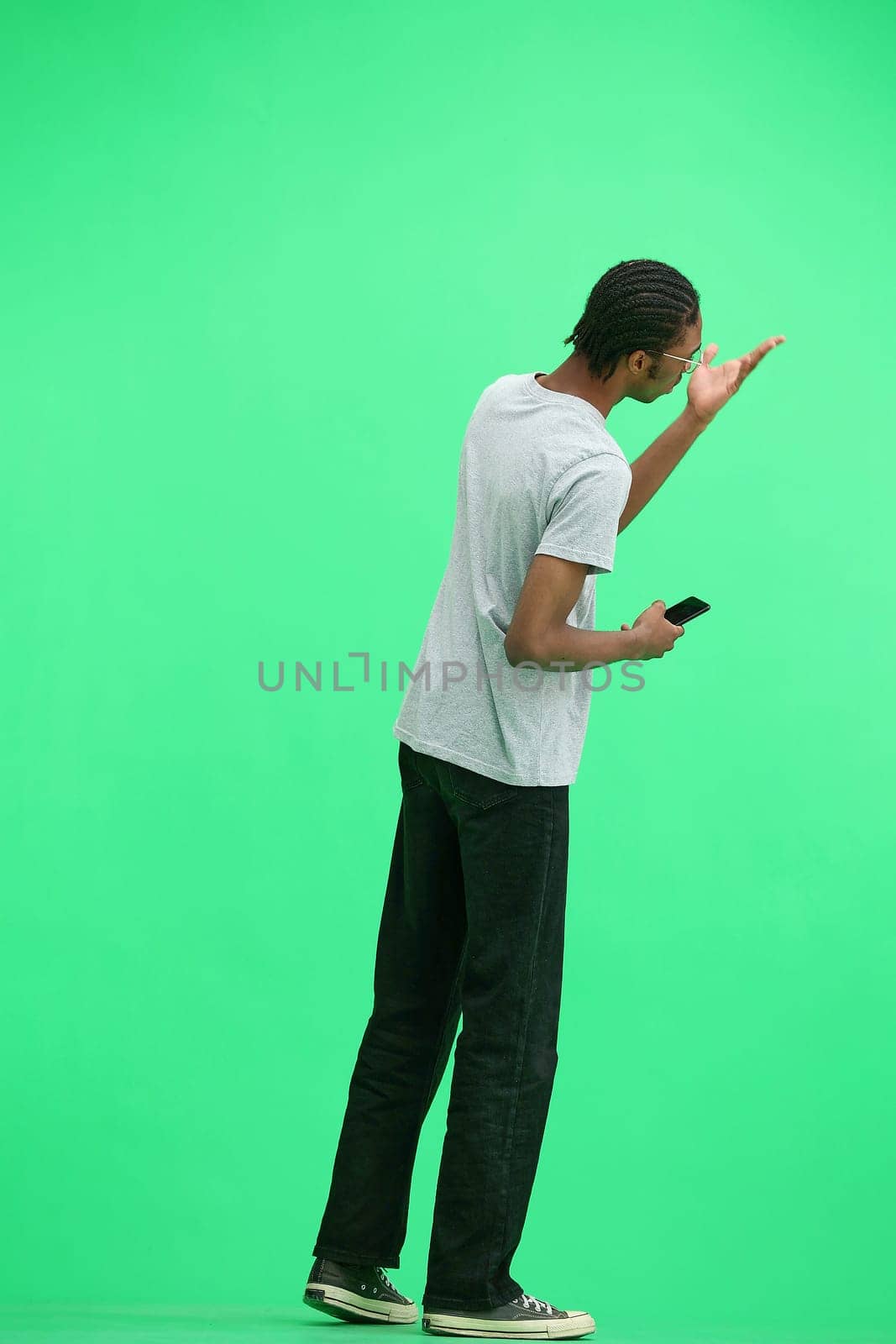 A man in a gray T-shirt, on a green background, full-length, with a phone.