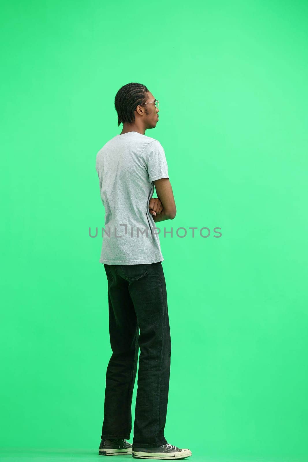 A man in a gray T-shirt, on a green background, in full height, crossed his arms.