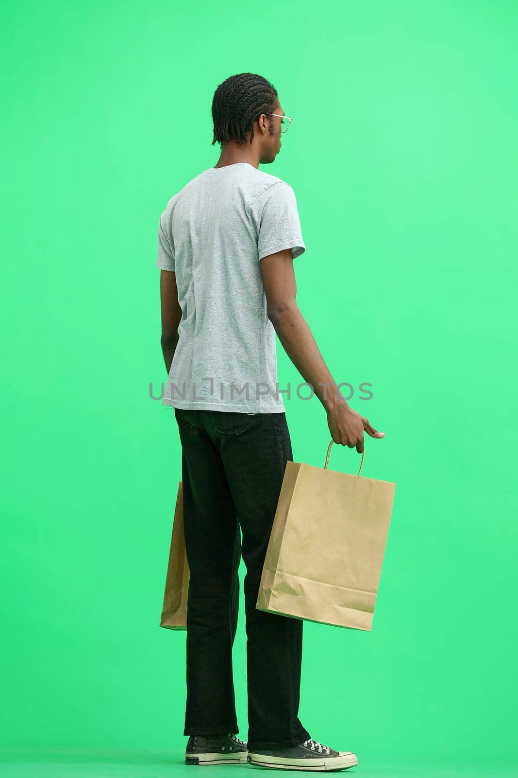 A man in a gray T-shirt, on a green background, full-length, with bags.