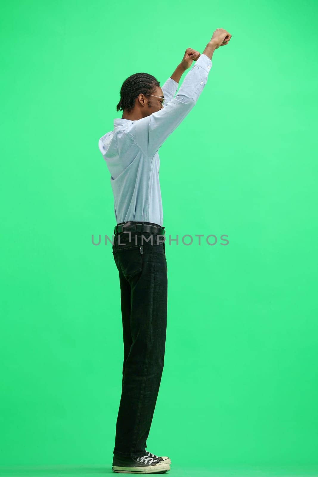 A man in a gray shirt, on a green background, in full height, raised his hands.