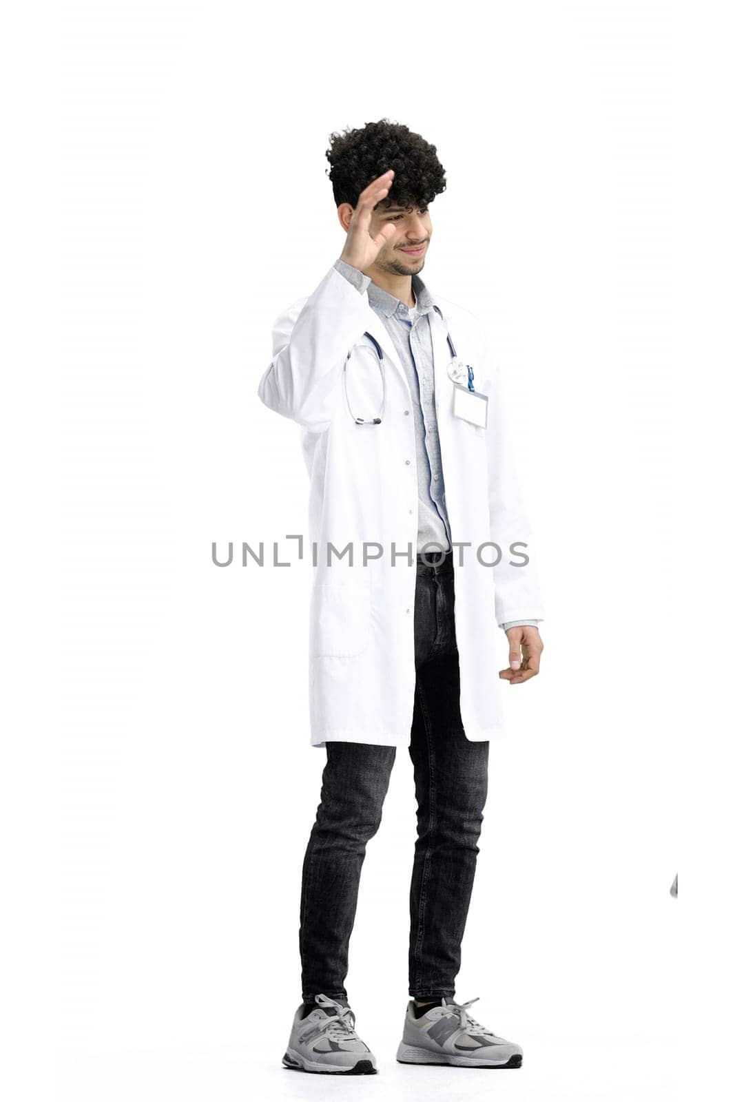 A male doctor, full-length, on a white background, waving his hand.