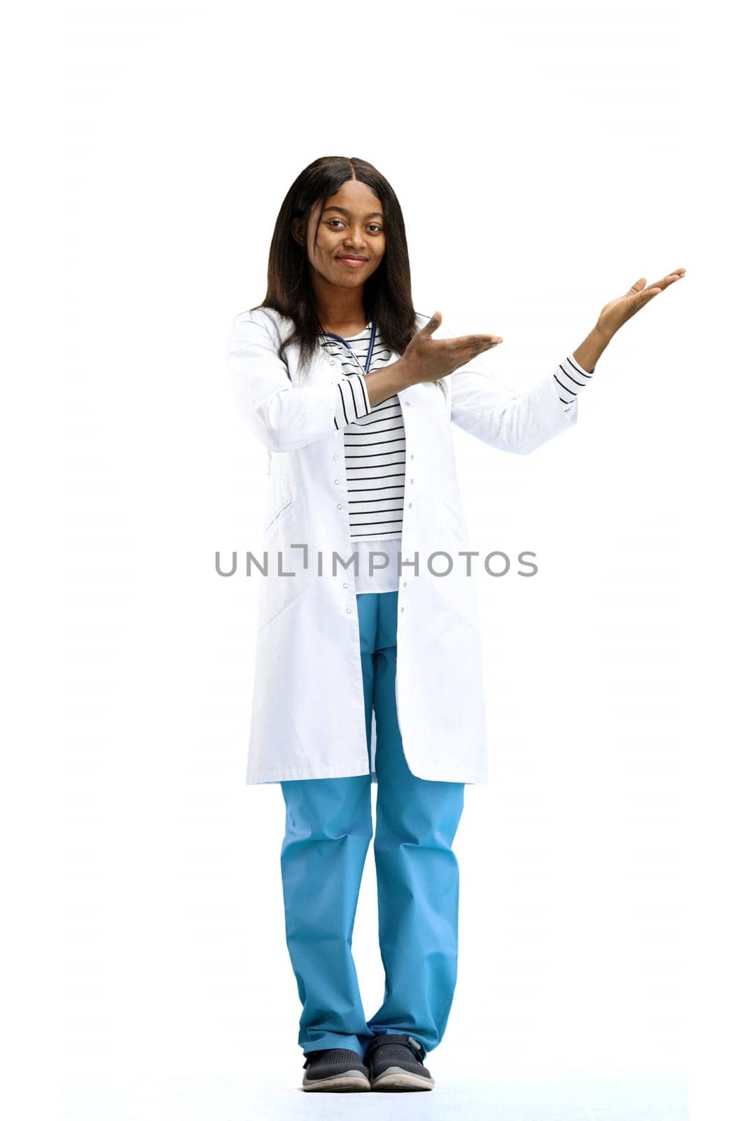 A female doctor, on a white background, in full height, points to the side.