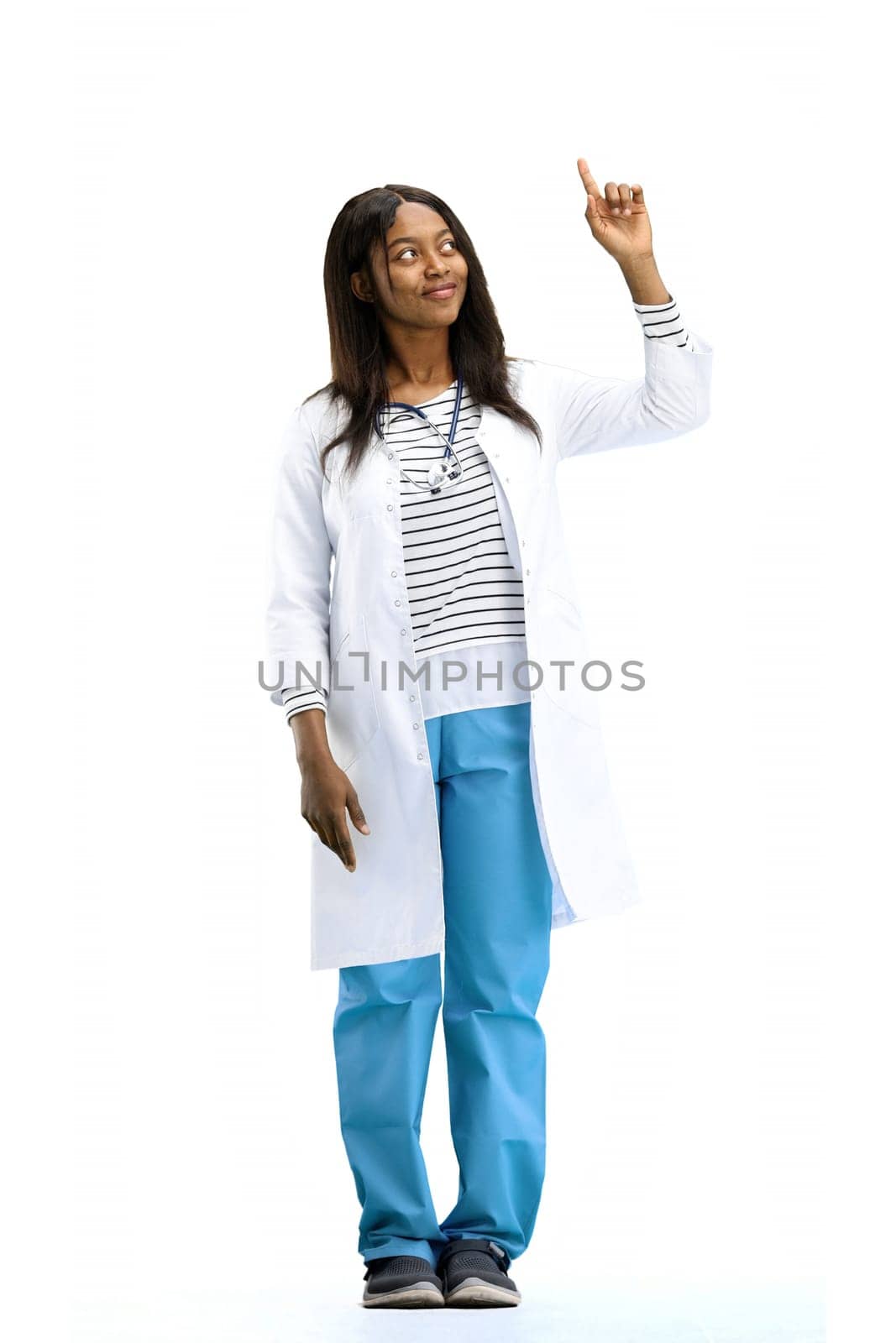 A female doctor, on a white background, in full height, points to the side.