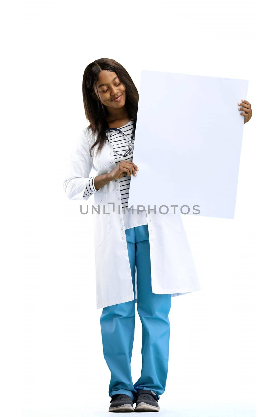 A female doctor, on a white background, in full height, shows a white sheet.