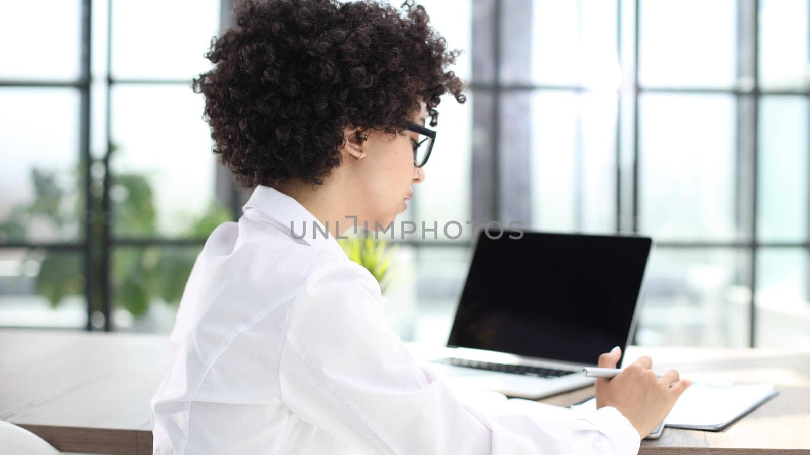 Image of young beautiful joyful woman smiling while working with laptop in office