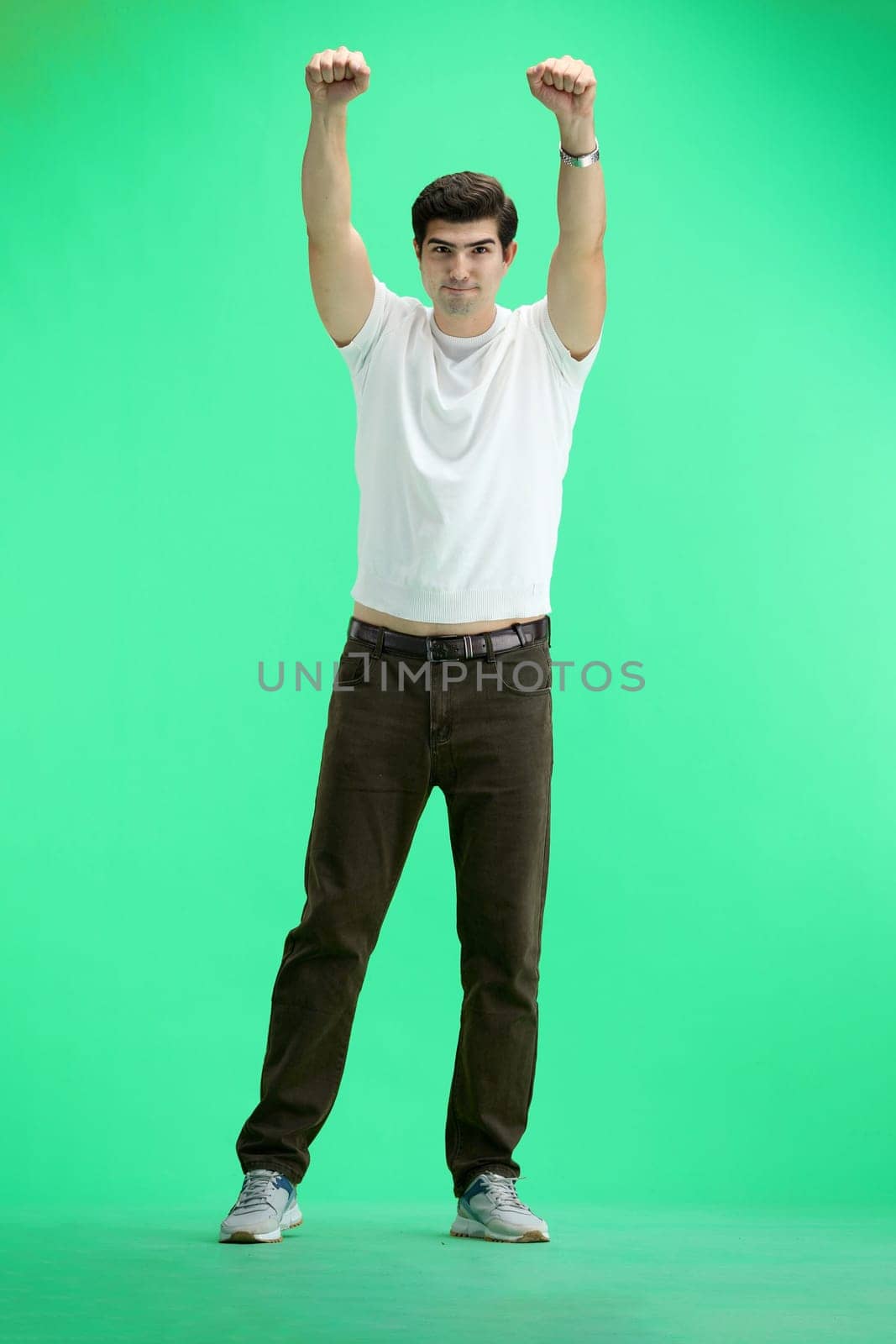 A man in full height, on a green background, raised his hands up.