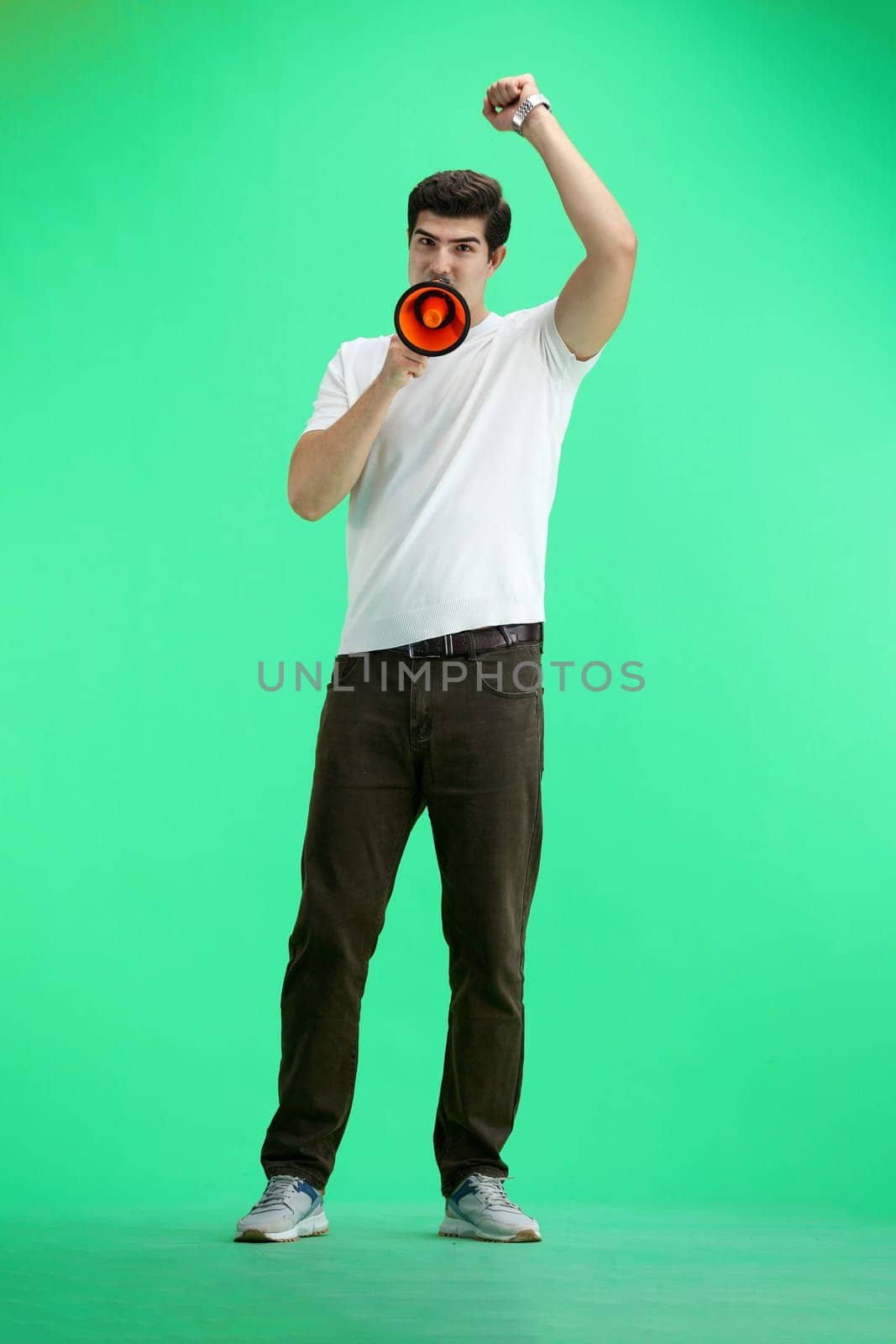 A man in full height, on a green background, with a megaphone.