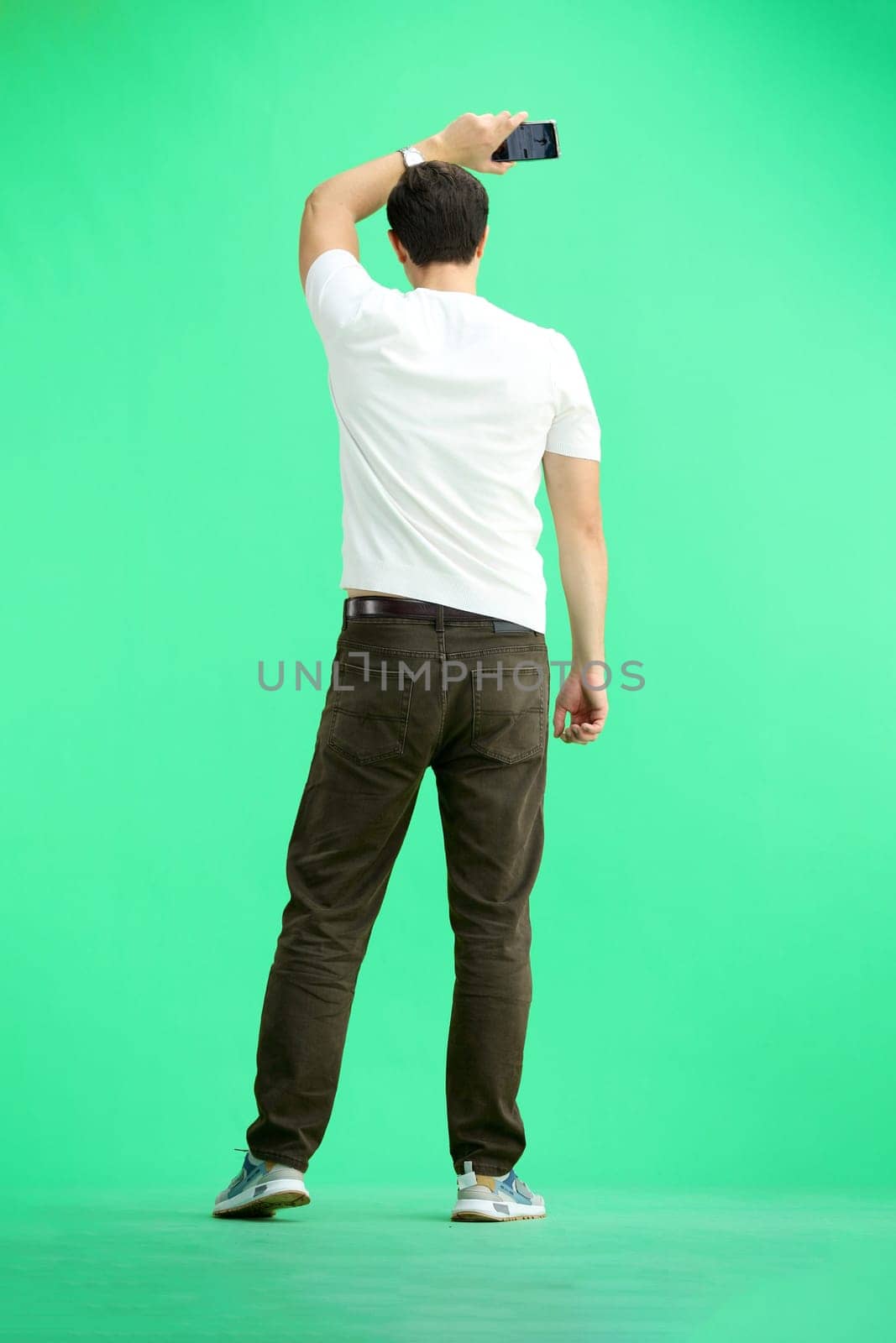 A man in full height, on a green background, waving his phone.