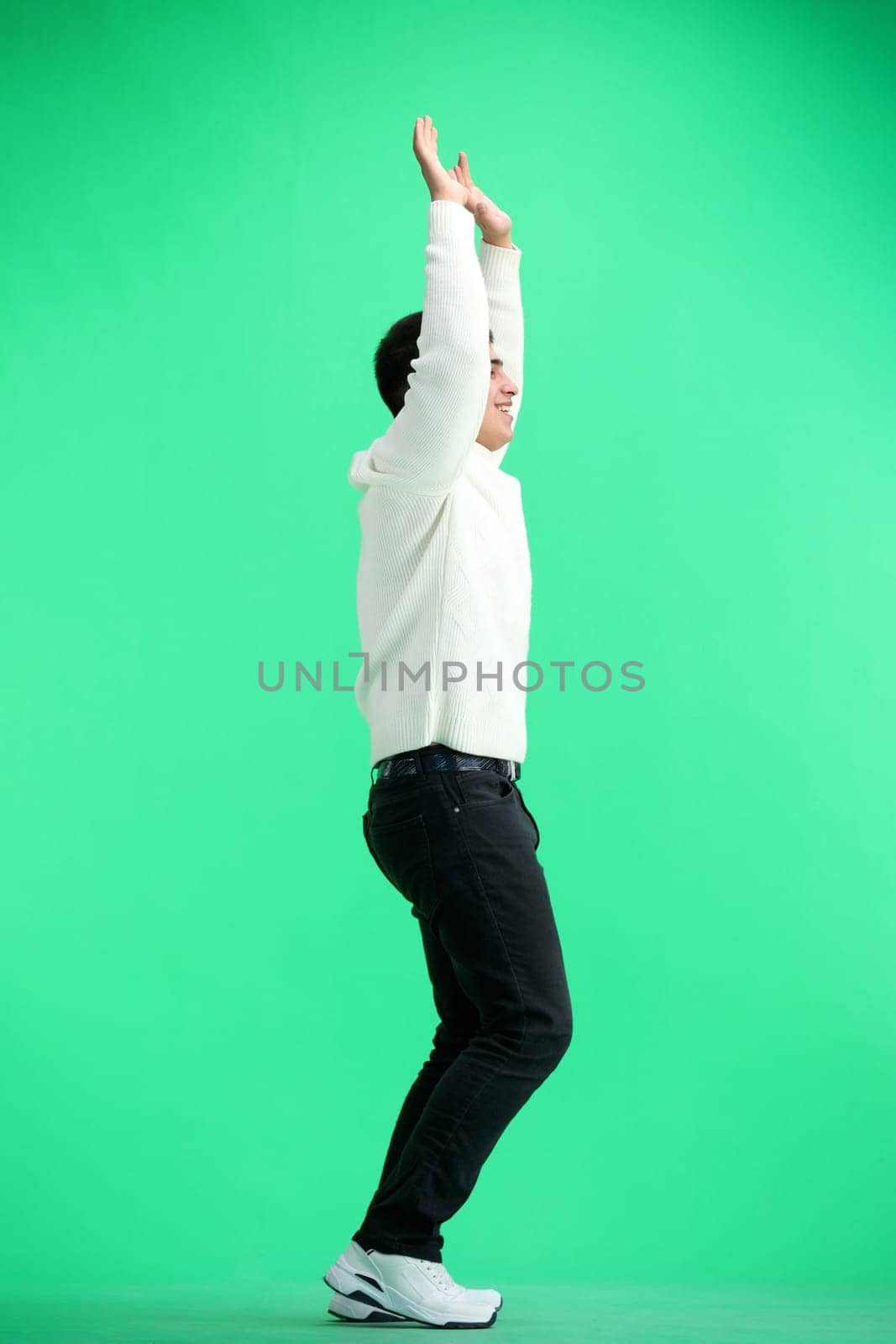 A man, full-length, on a green background, raised his hands up.