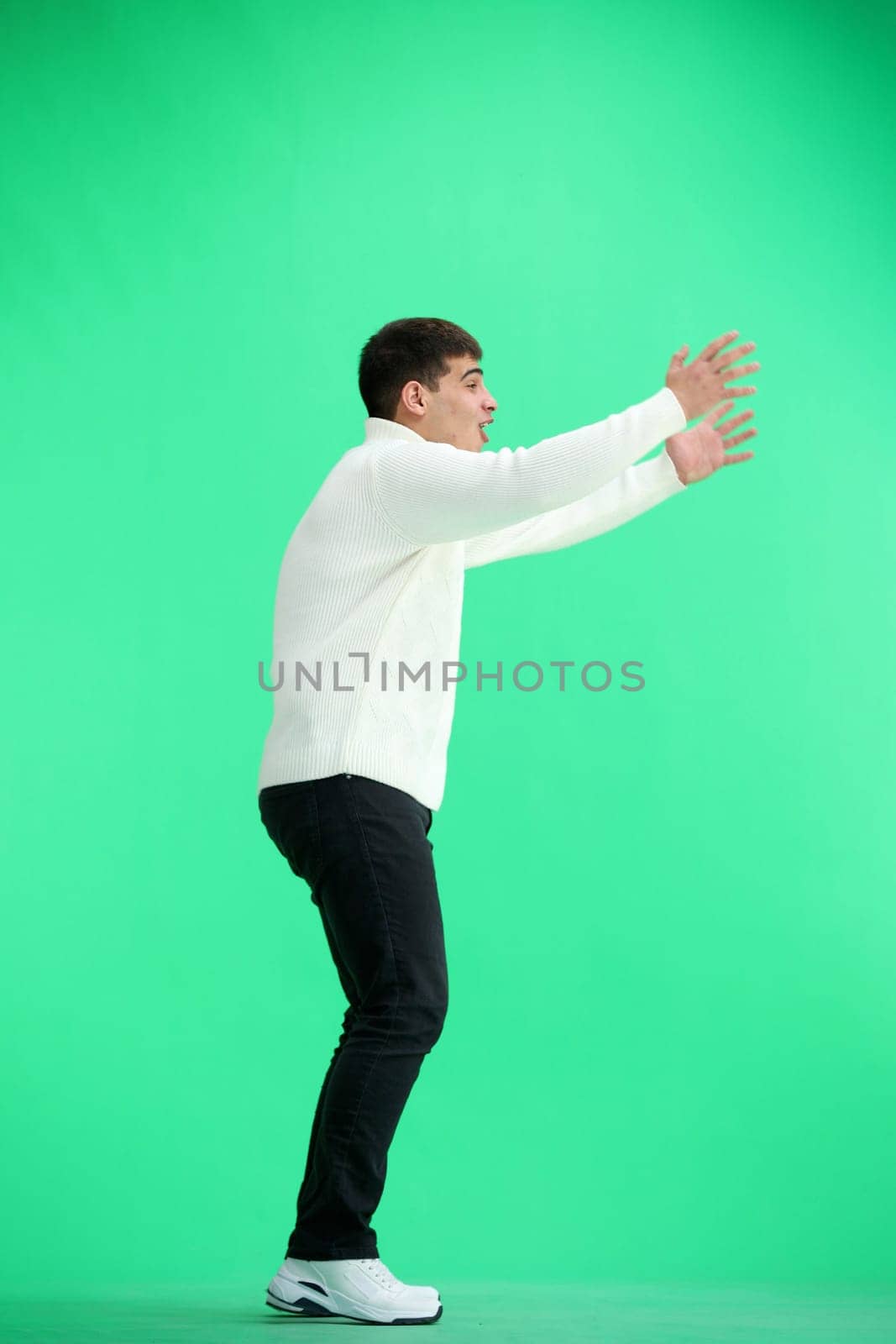 A man, full-length, on a green background, spreads his arms.