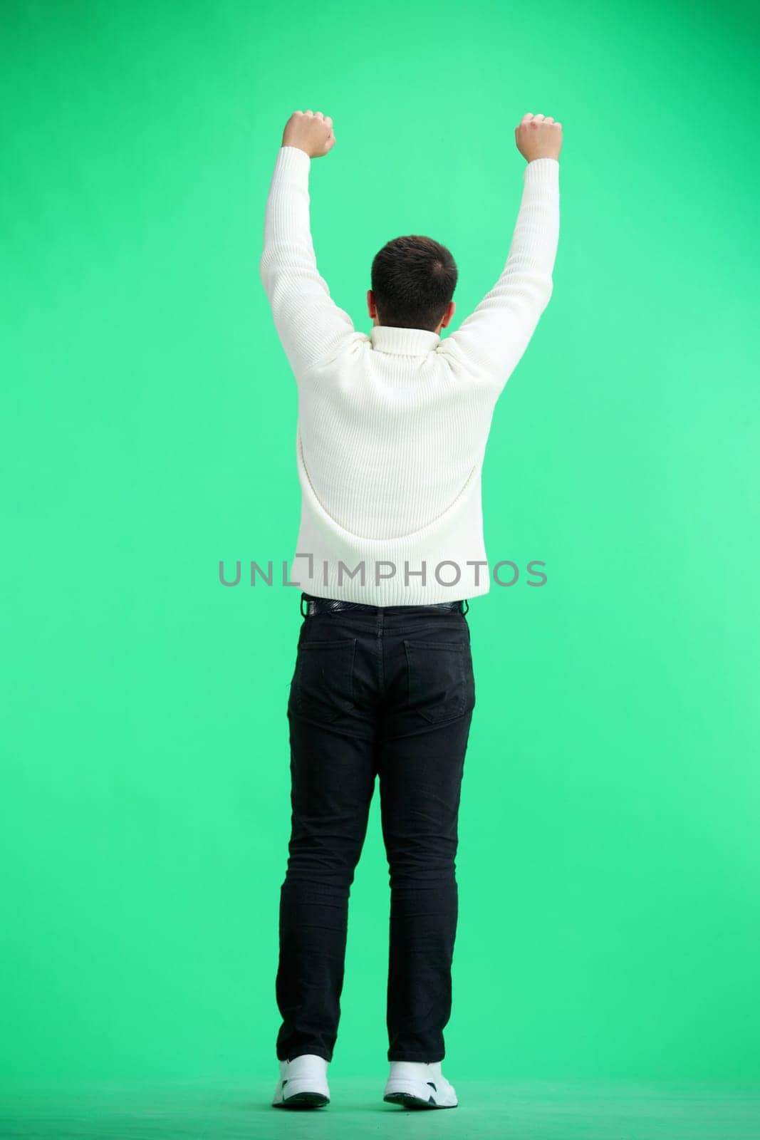 A man, full-length, on a green background, raised his hands up.