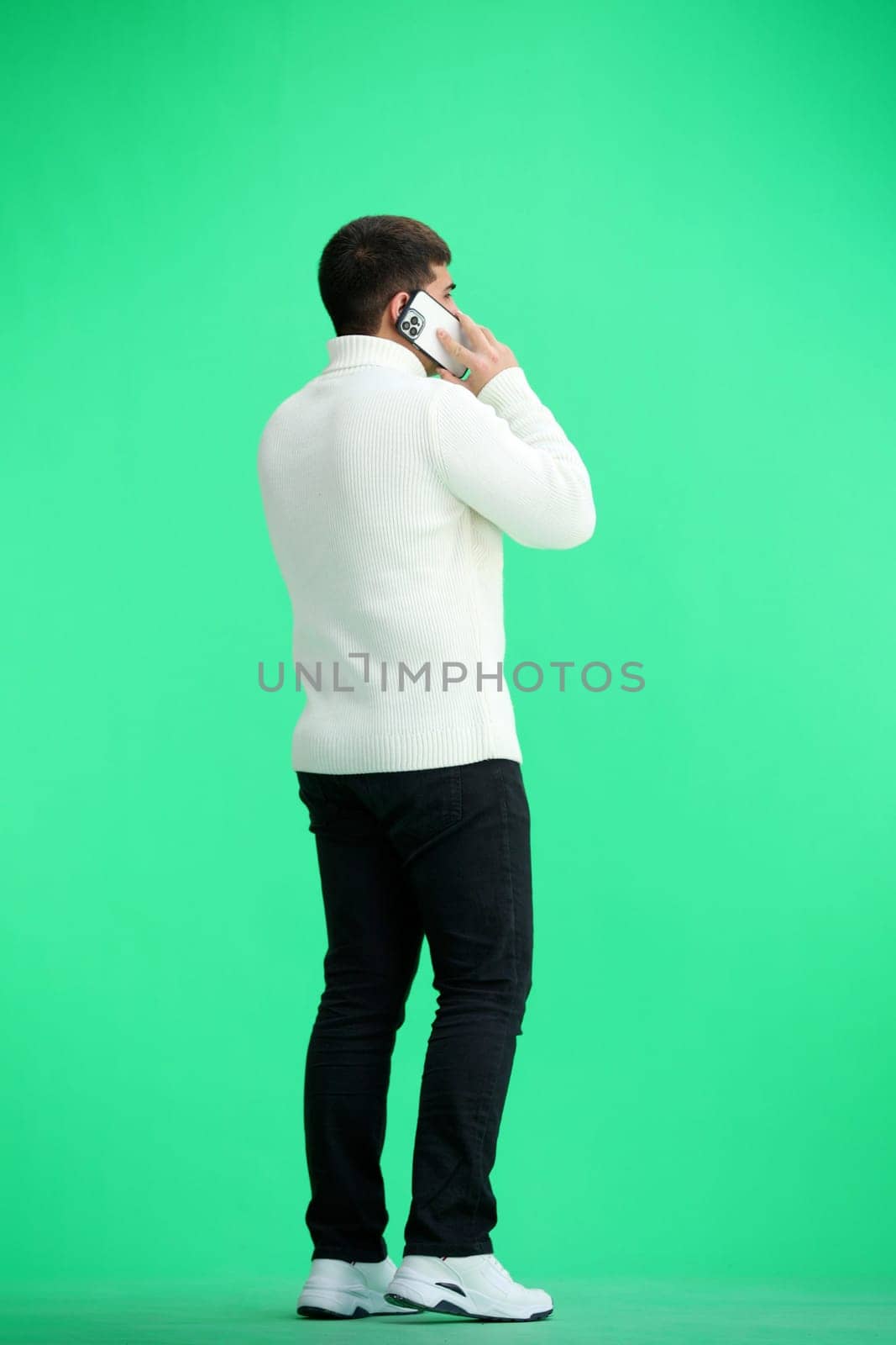 A man, full-length, on a green background, talking on the phone.