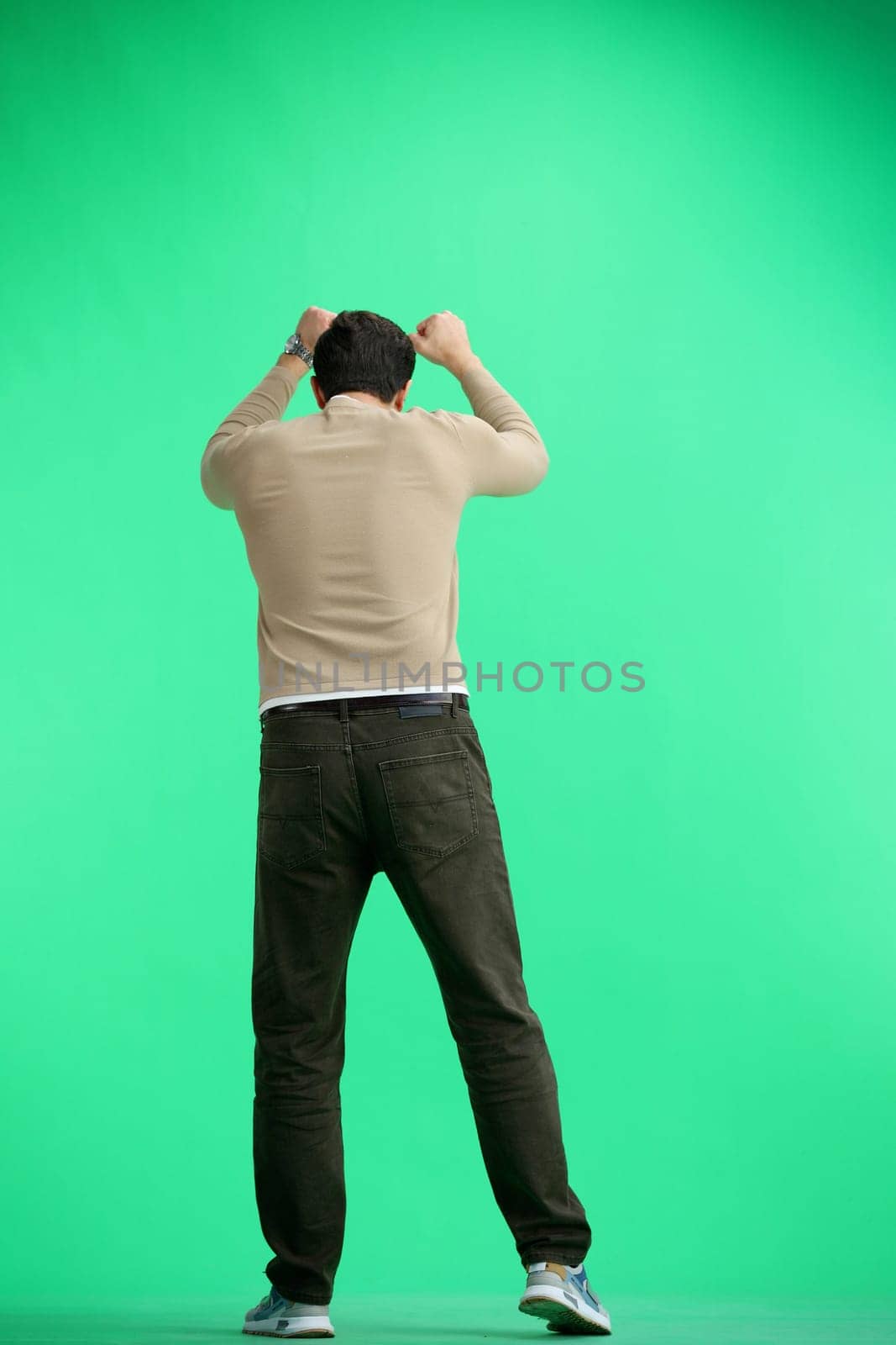 A man, full-length, on a green background, raised his hands up.