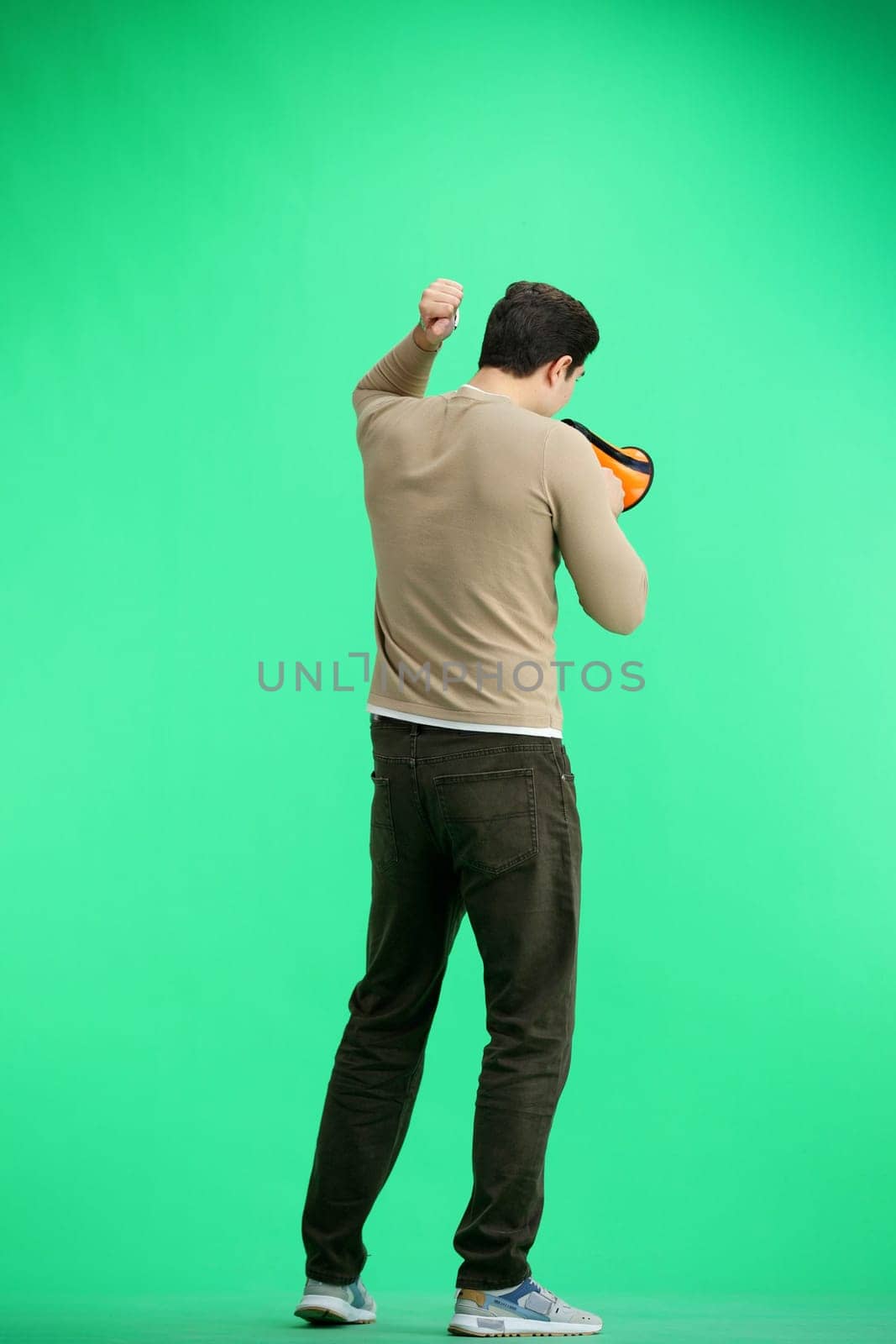 A man, full-length, on a green background, with a megaphone.