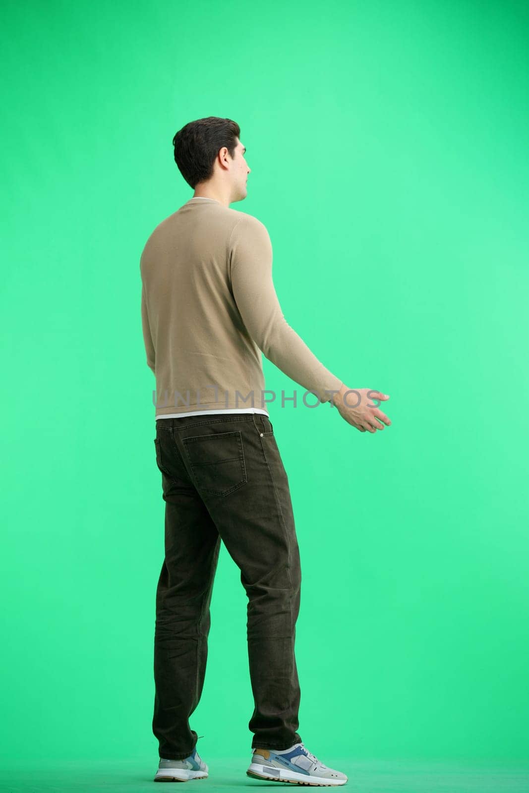 A man, full-length, on a green background, spreads his arms.