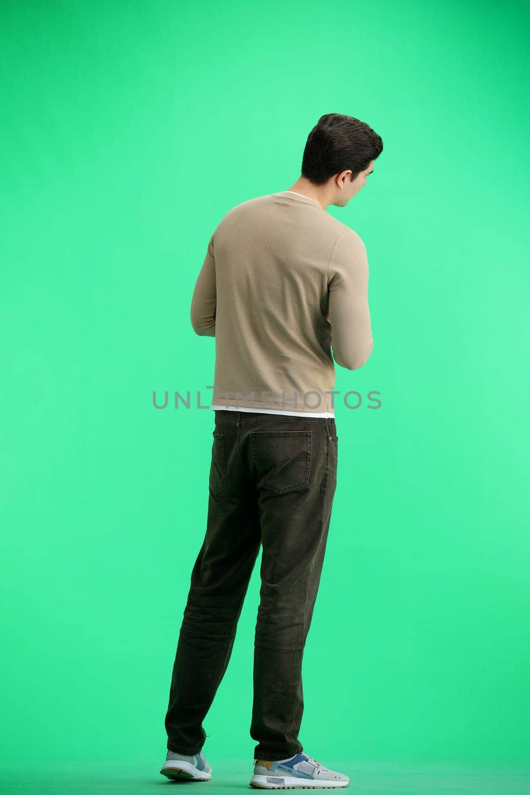 A man, full-length, on a green background, uses a phone.