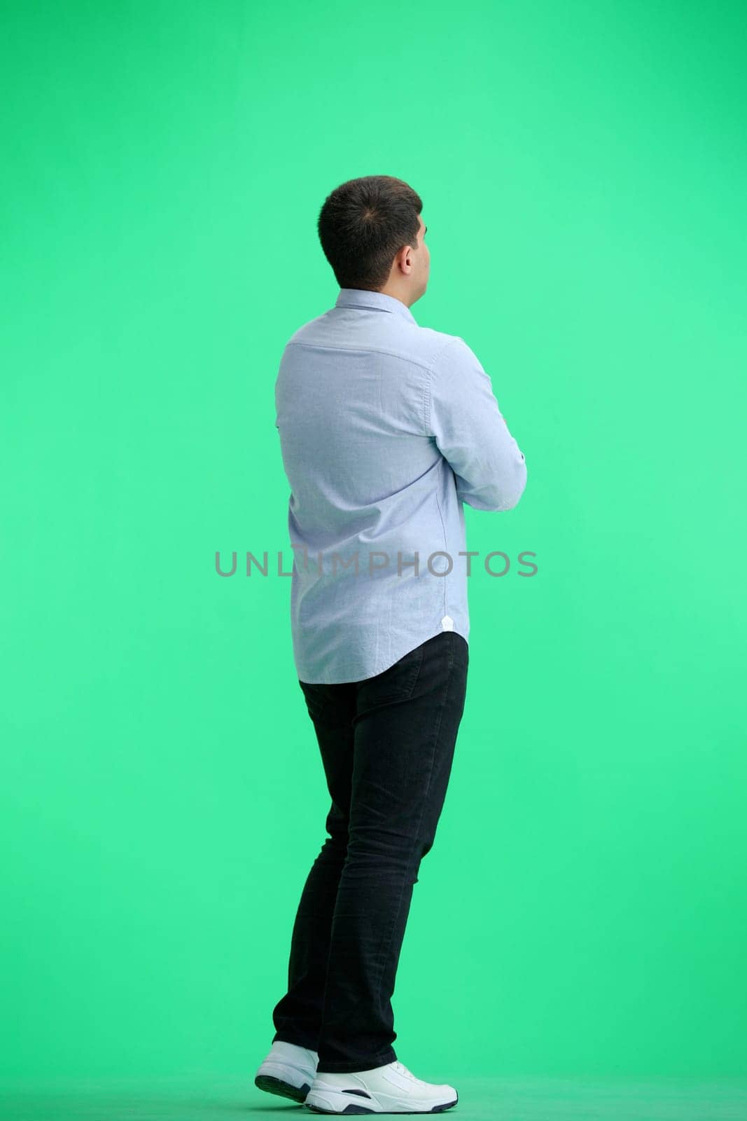 A man, full-length, on a green background, crossed his arms.