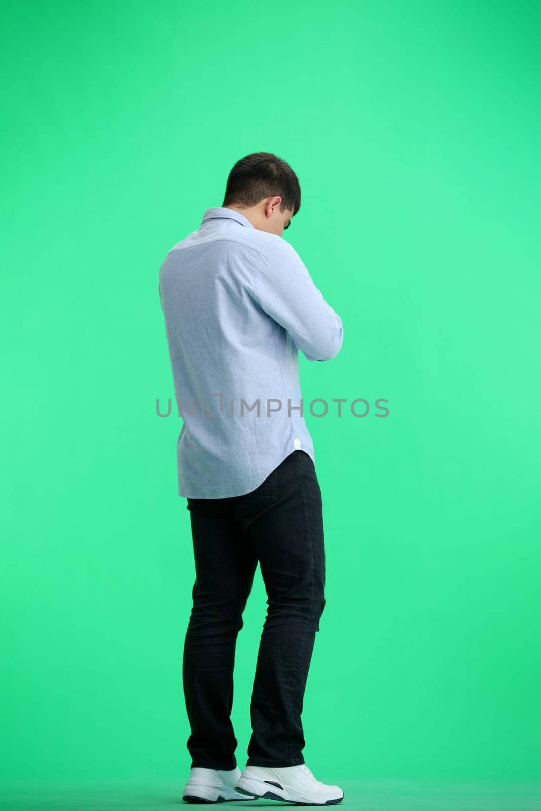 A man, full-length, on a green background, looks at his watch by Prosto