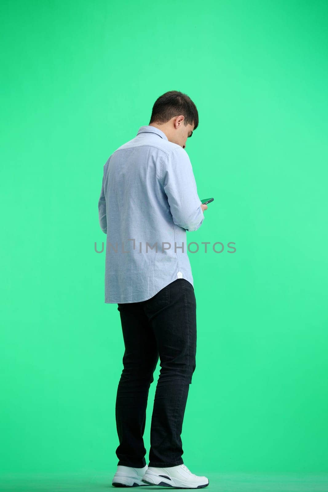 A man, full-length, on a green background, with a phone by Prosto