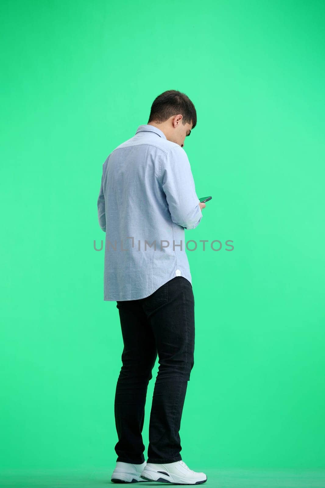 A man, full-length, on a green background, with a phone.