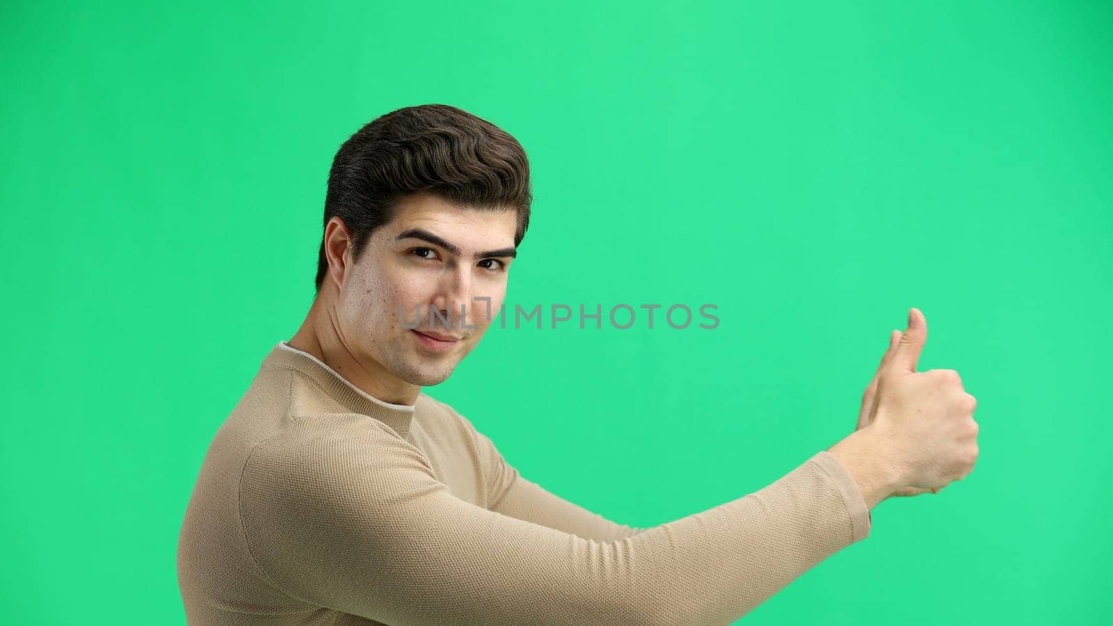 A man, close-up, on a green background, shows his thumbs up.