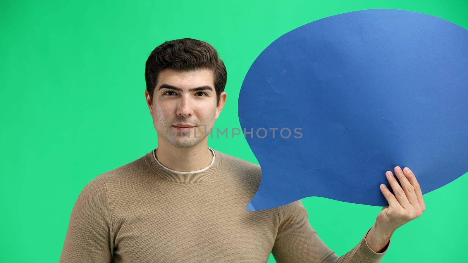 A man, close-up, on a green background, shows a blue comment sign by Prosto